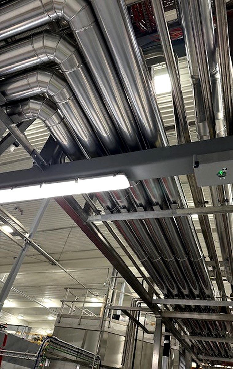 Overhead metal-clad pipe runs including bend and elbow fittings in an industrial warehouse